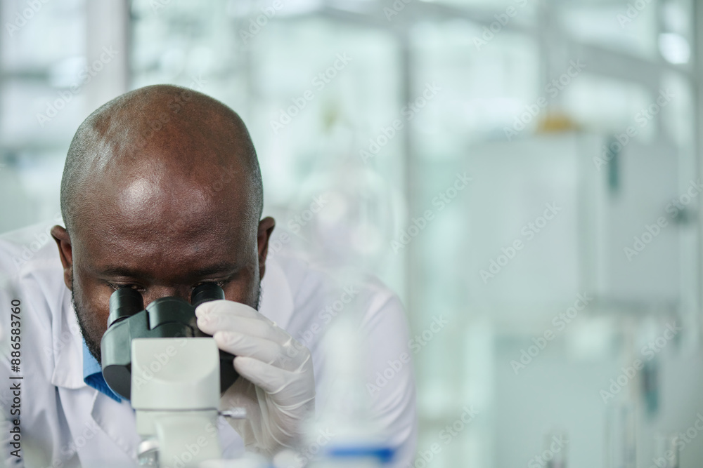 Poster bald african american male clinician in protective gloves studying new virus or variant in microscop