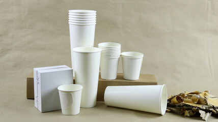White paper coffee cup, used paper, and cardboard box on a brown surface, awaiting recycling.