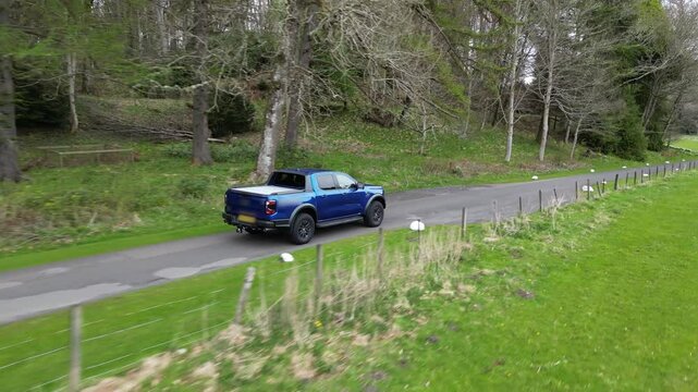 pick up truck driving on road remote landscape green fields barbed wire countryside forest trees side shot aerial generic unmarked
