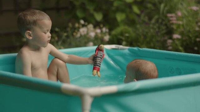 In green backyard two children gleefully soak up fun in inflatable pool playful funny. Positioned amidst vibrant greenery children in inflatable pool beckons children simple joys of childhood