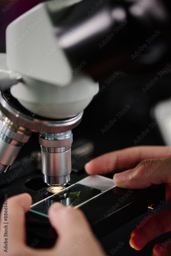 Poster hands of young unrecognizable researcher or chemist putting biotechnological sample under lens of mi