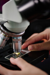 Fingers of young unrecognizable female virologist putting sample of new strain under lens of microscope before studying virus