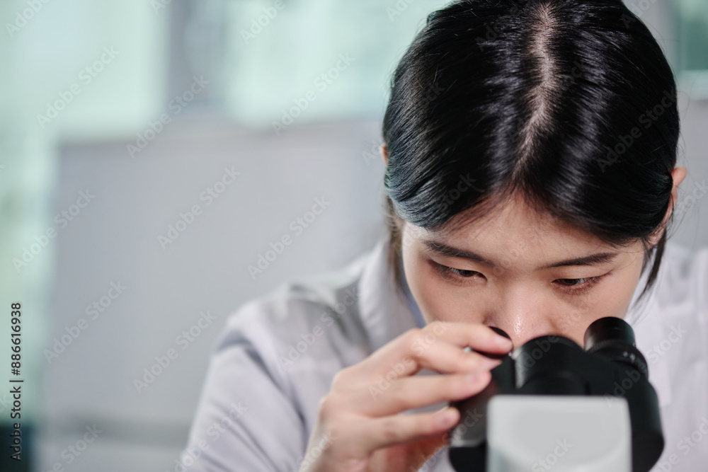 Poster young brunette chinese woman in lab coat sitting in front of camera and looking at new strain of vir