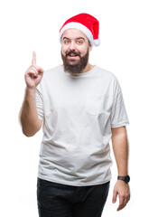 Young caucasian hipster man wearing christmas hat over isolated background pointing finger up with successful idea. Exited and happy. Number one.