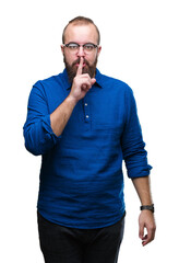 Young caucasian hipster man wearing glasses over isolated background asking to be quiet with finger on lips. Silence and secret concept.