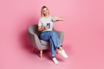 Photo of positive adorable girl wear stylish grey clothes sit comfy chair thumb up isolated on pink color background