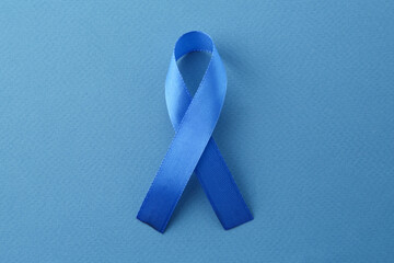 Blue awareness ribbon on color background, top view