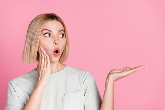 Portrait of astonished girl with bob hairstyle wear white t-shirt staring at product on arm empty space isolated on pink color background