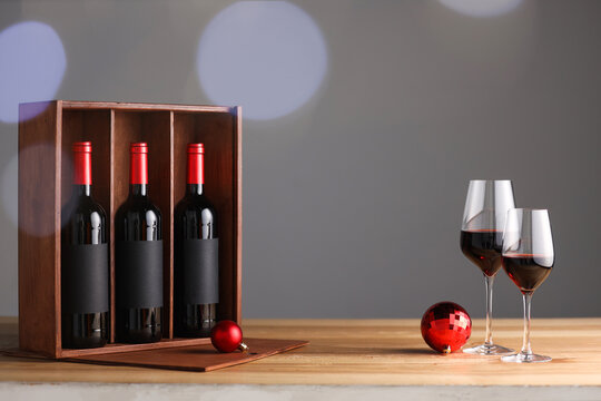 Wooden gift box with bottles of wine, glasses and red Christmas balls on table, space for text
