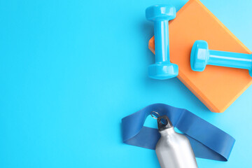Two dumbbells, yoga block, fitness elastic band and thermo bottle on light blue background, flat lay. Space for text