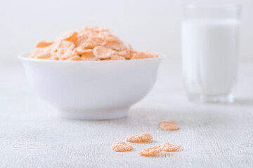 bowl of corn granola with milk, fresh raspberries, blueberries . milk in a jug and a glass  on white wooden board for healthy breakfast