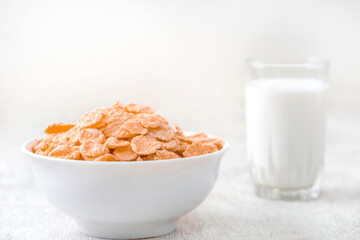 bowl of corn granola with milk, fresh raspberries, blueberries . milk in a jug and a glass  on white wooden board for healthy breakfast