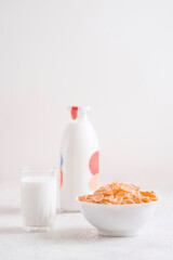 bowl of corn granola with milk, fresh raspberries, blueberries . milk in a jug and a glass  on white wooden board for healthy breakfast