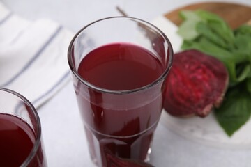 Fresh beet juice in glasses, ripe vegetable and basil on light table, closeup