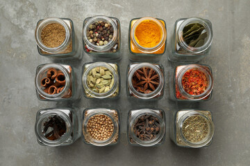 Different spices in glass jars on grey table, flat lay