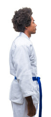Afro american man wearing karate kimono over isolated background looking to side, relax profile pose with natural face with confident smile. © Krakenimages.com