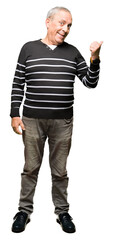 Handsome senior man wearing winter stripes sweater smiling with happy face looking and pointing to the side with thumb up.