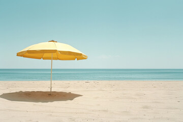 A lone yellow beach umbrella stands on an empty, sandy shore against a serene ocean backdrop
