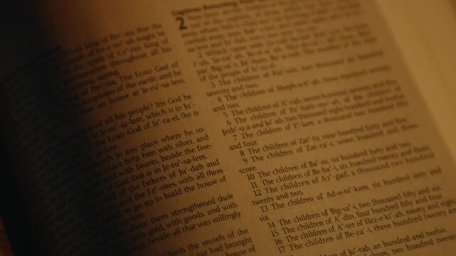 Opened paper Bible on a desk, in soft candle light, candle is burning nearby, holy scripture, High quality 4k footage