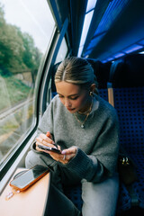 Attractive caucasian woman using a smartphone in regional train. Young beautiful woman using public transportation.