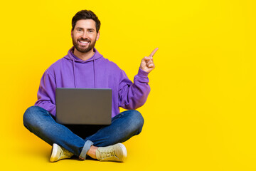 Full body photo of attractive young man point empty space netbook dressed stylish violet clothes isolated on yellow color background