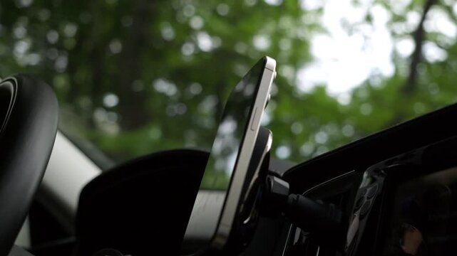 mobile phone is attached to a dashboard while a car is driving along a country road with a forest in the background.