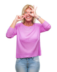 Middle age blonde woman eatin pink macaron biscuit over isolated background with happy face smiling doing ok sign with hand on eye looking through fingers