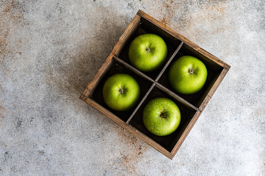 Overhead view of four green apples in a wooden box on a table