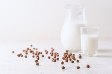 Milk in a glass and chocolate balls on a light background.