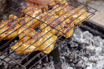 An elderly man grills chicken with the embers of a campfire, creating an appetizing and traditional outdoor barbecue. Experience with a traditional BBQ setup.