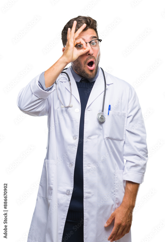 Wall mural Young handsome doctor man over isolated background doing ok gesture shocked with surprised face, eye looking through fingers. Unbelieving expression.