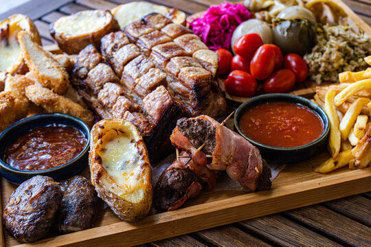 Close-up of roasted pork with crackling, fried chicken, meatballs, sausages wrapped in bacon, potatoes stuffed with cheese and chips with barbecue sauce