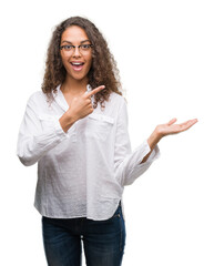 Beautiful young hispanic woman amazed and smiling to the camera while presenting with hand and pointing with finger.