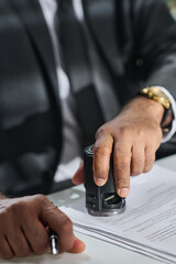 Hand of mature unrecognizable male lawyer or solicitor putting stamp on contract or other paper...