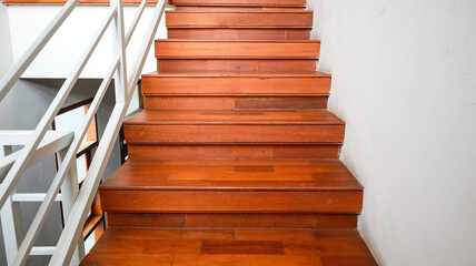 Close-up view of a modern wooden staircase with a white handrail. The staircase is lit by natural light, creating a bright and clean atmosphere. Wooden Staircase Interior Design