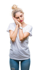 Fototapeta premium Young beautiful blonde woman wearing white t-shirt over isolated background sleeping tired dreaming and posing with hands together while smiling with closed eyes.