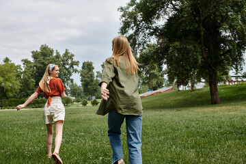 Obraz premium Two young women, dressed casually, run through a green park during a summer afternoon.