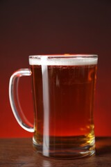 Mug with fresh beer on wooden table against color background, closeup