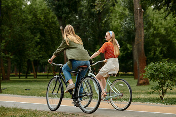 Fototapeta premium Two young women on a bicycle date, enjoying a sunny day in a park.