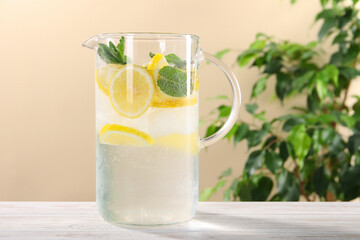 Freshly made lemonade with mint in jug on white wooden table against beige background