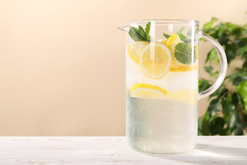 Freshly made lemonade with mint in jug on white wooden table against beige background, space for text