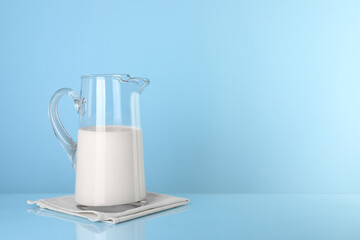 Glass jug of fresh milk on light blue background, space for text