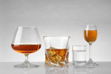 Glasses with different alcoholic drinks on white table against light background
