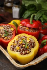 Quinoa stuffed bell peppers and basil in baking dish on wooden table, closeup
