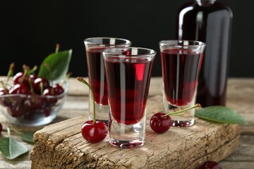 Bottle and shot glasses of delicious cherry liqueur with juicy berries on wooden table