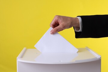 Woman putting her vote into ballot box against yellow background, closeup