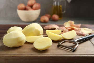 Fresh raw potatoes, peels and peeler on table