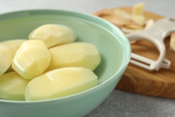 Fresh raw potatoes in bowl on light grey table, closeup
