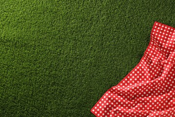 Checkered picnic tablecloth on green grass, top view. Space for text
