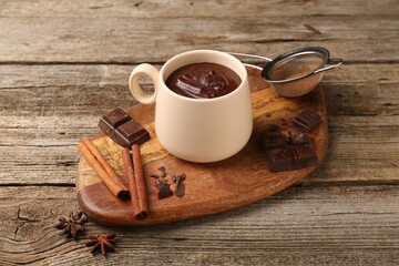 Tasty melted chocolate in cup and spices on wooden table, closeup